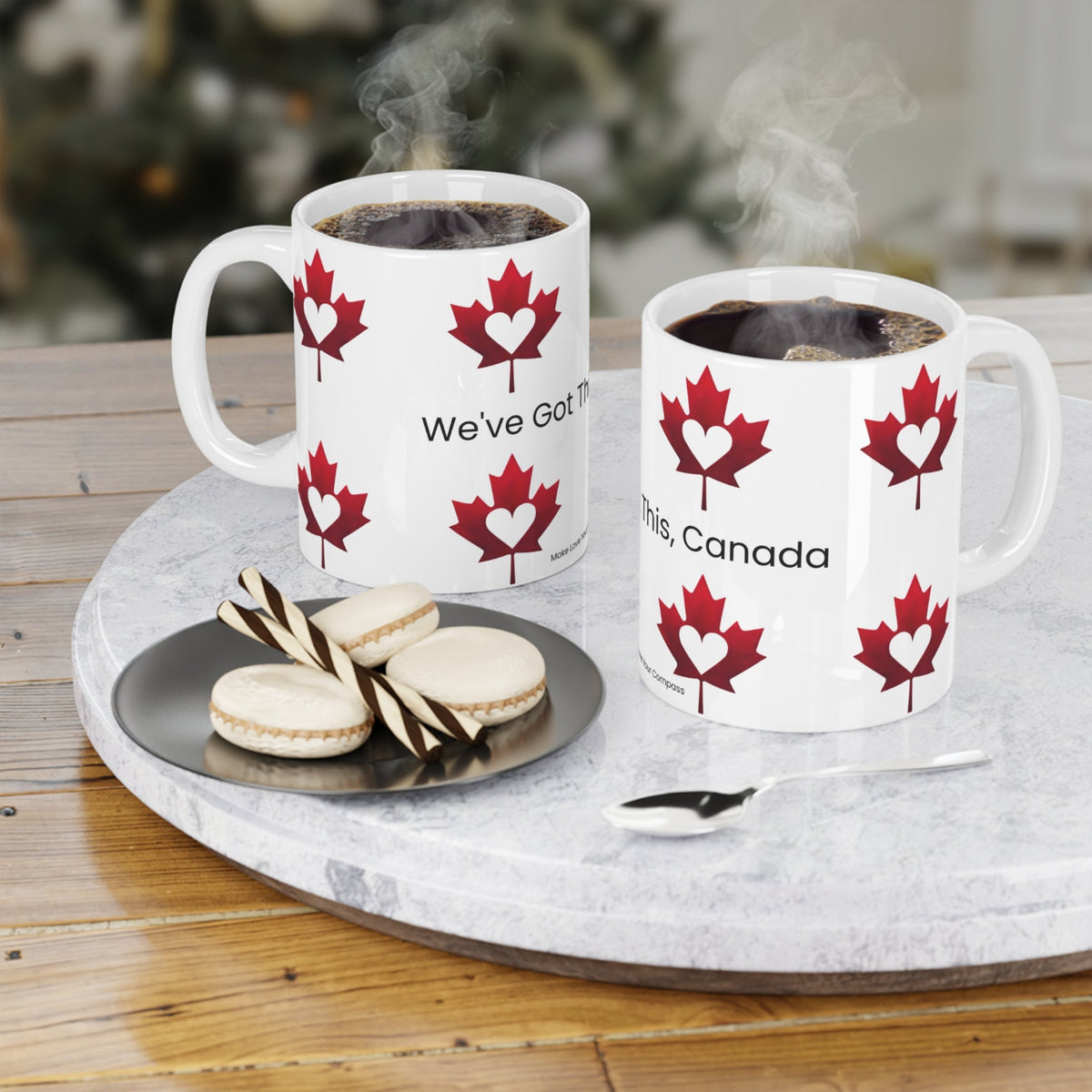 Two mugs with red maple leaf designs on a tray with cookies and a spoon.