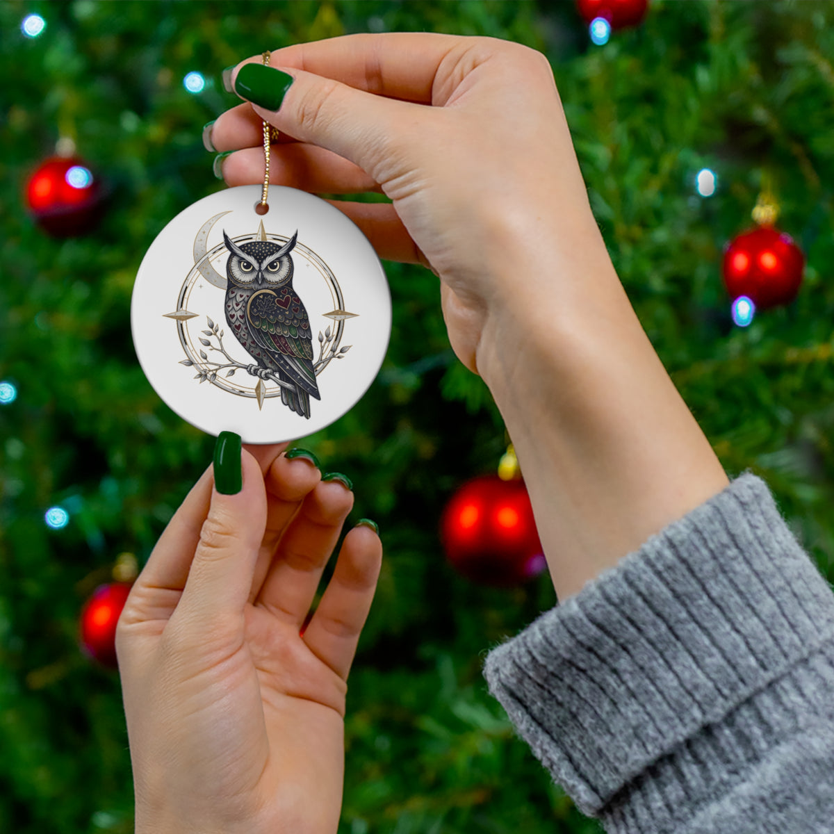 Make Love Your Compass Owl Ornament: A woman holding the white ceramic ornament with both hands to showcase the owl and crescent moon design, with a beautifully decorated Christmas tree in the background.