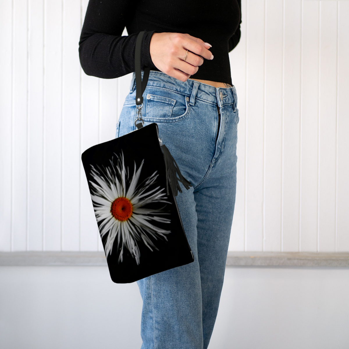 Person holding a black pouch with a white flower design against a white background