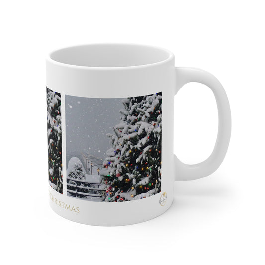 A white ceramic mug featuring a printed winter holiday photograph of snow-covered Christmas trees with colorful lights, on a clean white background.