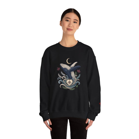 Make Love Your Compass Whale Moon Sweatshirt: A female model wearing a black crewneck featuring a graphic print of a blue and white whale with a crescent moon and swirling waves against a white background.