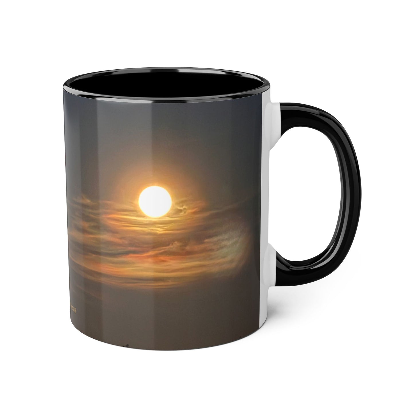 A ceramic mug with a black handle and interior, featuring a printed sunset design on the exterior. The design shows a bright moon over multi coloured clouds.