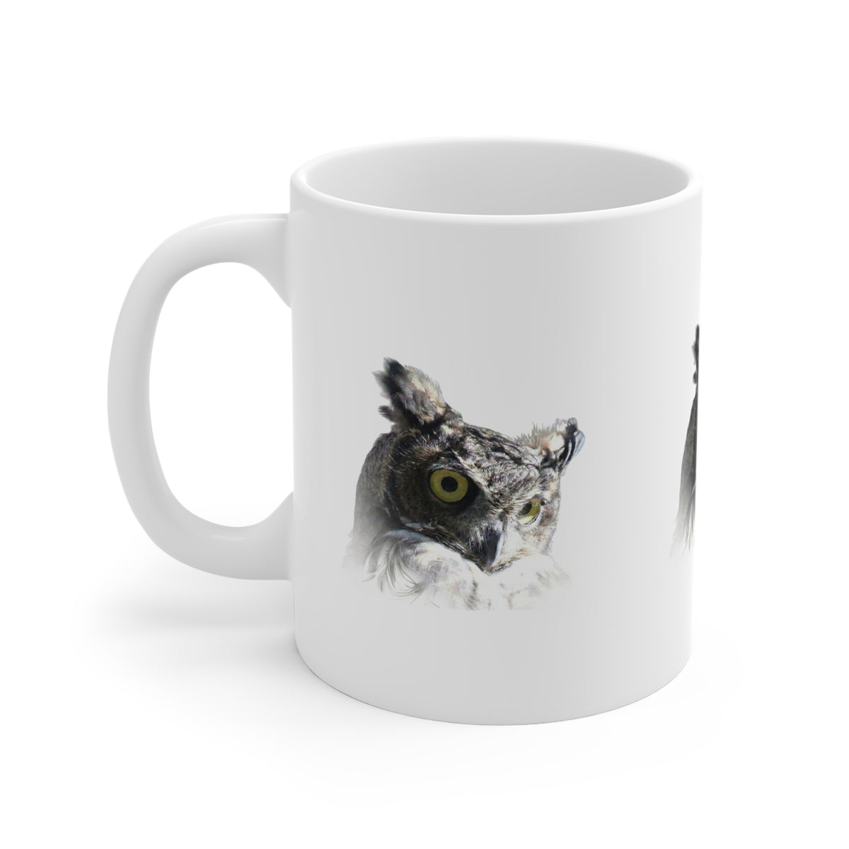 A white ceramic mug featuring a printed graphic of a great horned owl with a yellow eye, shown on a clean white background.