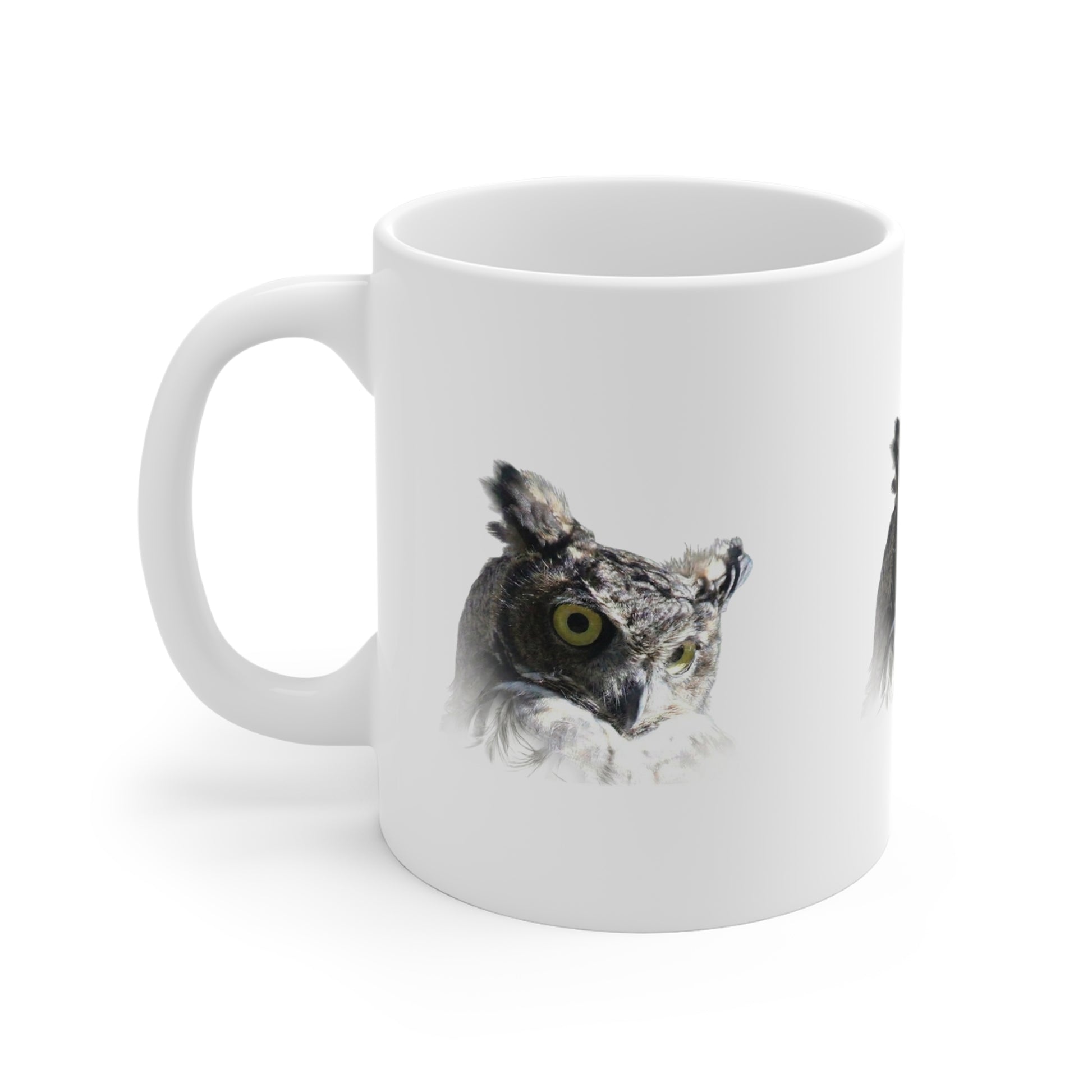 A white ceramic mug featuring a printed graphic of a great horned owl with a yellow eye, shown on a clean white background.