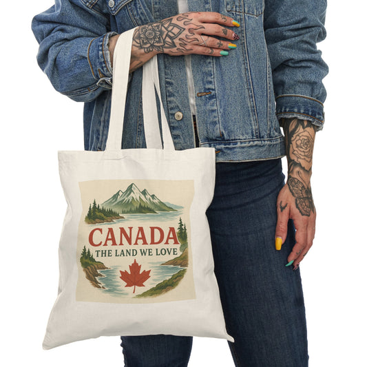 Tote bag with 'Canada, The Land We Love' design held by a person wearing a denim jacket.
