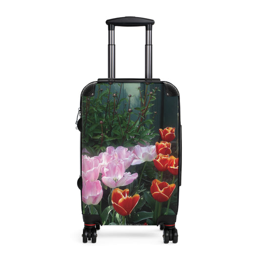 A hard-shell rolling suitcase with an extended black telescoping handle and four spinner wheels, featuring a printed floral design of pink tulips and red-orange tulips on a dark green background.