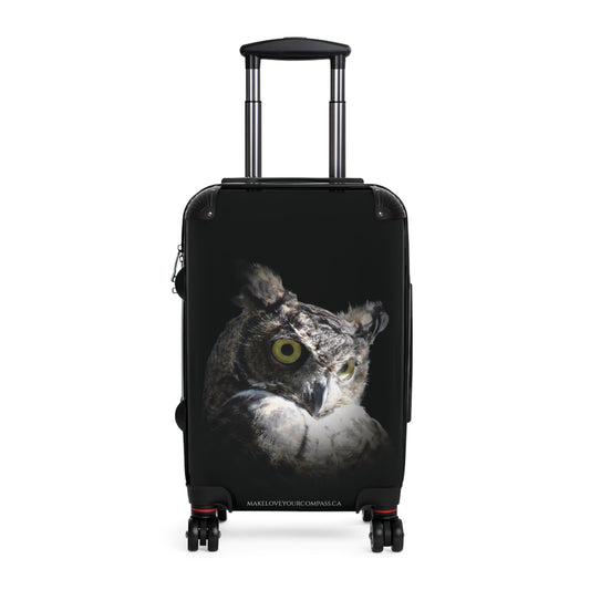 A black hard-shell rolling suitcase with an extended telescoping handle and four spinner wheels, featuring a Great Horned Owl face Original photo on the front. The suitcase is photographed against a solid white background.