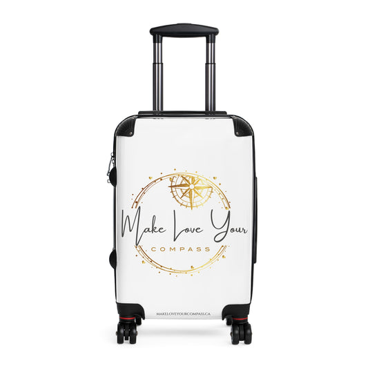 A white hard-shell spinner suitcase with an extended black telescoping handle and four wheels, featuring a gold compass graphic and the text 'Make Love Your Compass' printed on the front.