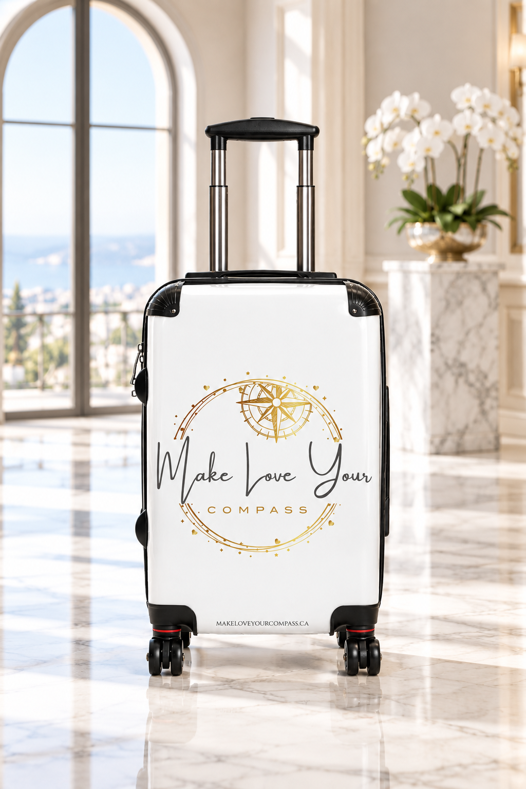 A white hard-shell spinner suitcase with an extended black telescoping handle and four wheels, featuring a gold compass graphic and the text 'Make Love Your Compass' printed on the front.