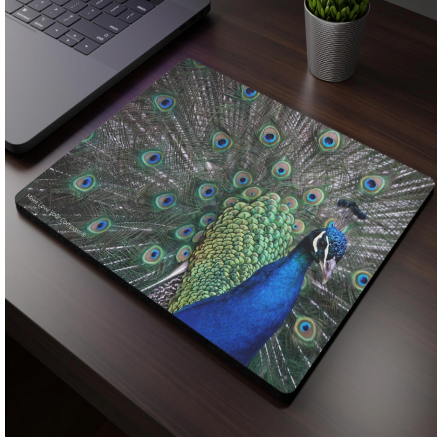 Mouse pad with peacock design on a desk next to a laptop